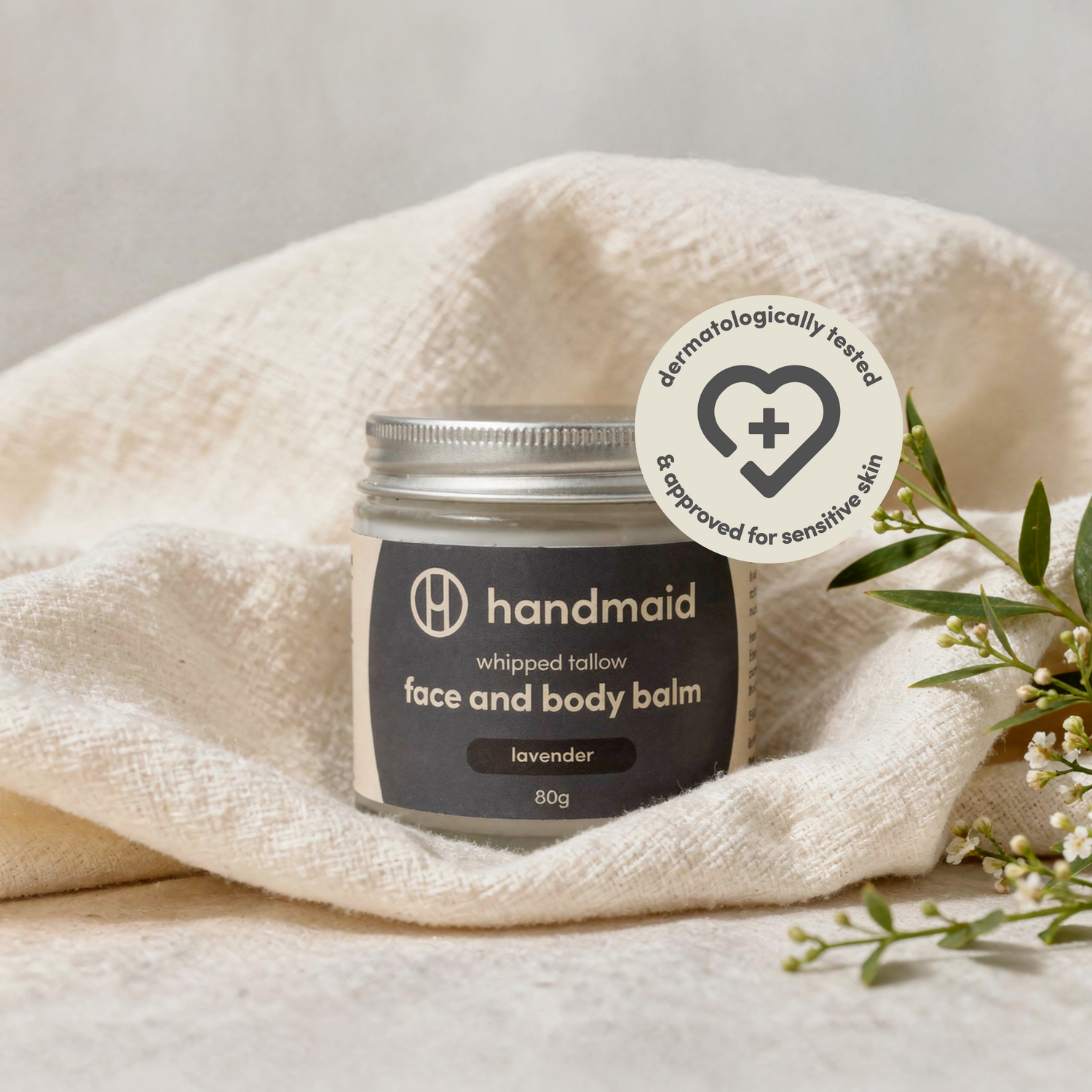 Jar of handmaid face and body balm on a white towel with a heart icon and text.