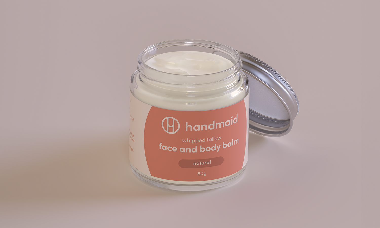 Jar of whipped balm with 'handmaid' label on a beige background