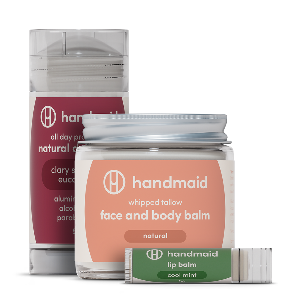Three jars of Handmaid brand skincare products, including a face and body balm, natural deodorant, and lip balm.