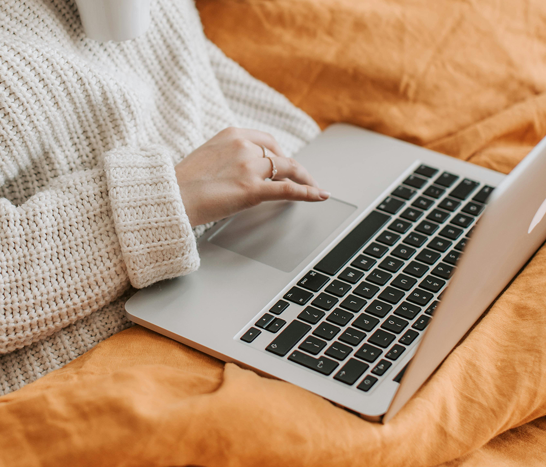 A person using a laptop on an orange blanket, browsing a tallow skincare and wellness blog.