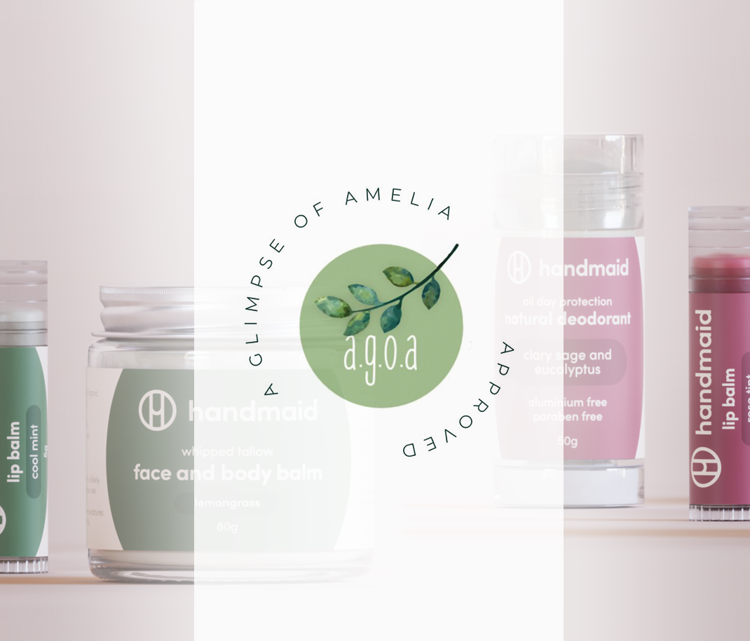 A promotional banner for Handmaid skincare products featuring the "A.G.O.A approved" certification stamp by Amelia Davatzis. The image displays a collection of natural skincare products, including face and body balm, natural deodorant, and lip balms, alongside text stating that the products are free from synthetic fragrances, preservatives, parabens, and PEGs.